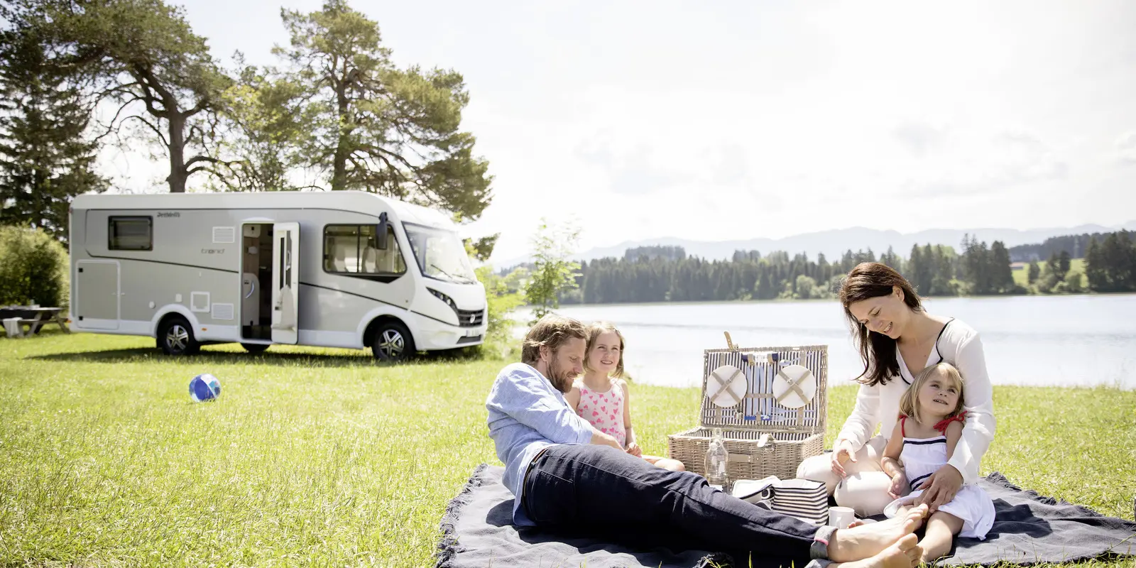  Family camping picnic by a lake beside a motorhome RV on a sunny grassy campsite