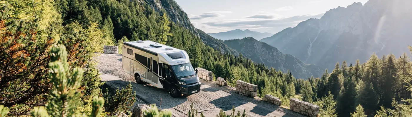 Camper van on a mountain road overlooking an alpine valley and forested peaks