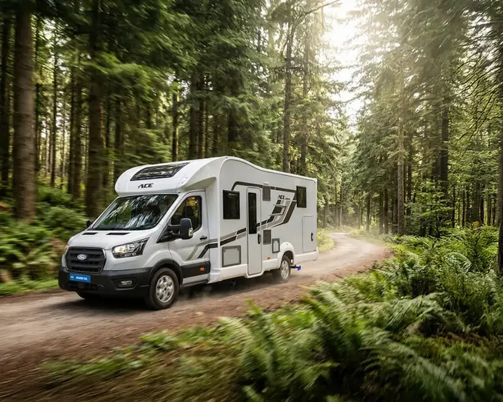 White camper van driving on a forest dirt road surrounded by tall evergreen trees
